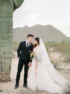 a bride and groom standing in front of a cactus