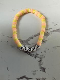 "this is a pink, bright yellow, and light yellow. clay beaded braclet made by me! It says \"aloha\" on it, Which means hello!" Colorful Beaded Yellow Bracelets For Vacation, Adjustable Yellow Friendship Bracelets With Letter Beads, Yellow Beaded Bracelets For Vacation, Yellow Beaded Bracelet For Vacation, Yellow Bracelets With Round Beads For Vacation, Fun Yellow Beaded Bracelets For Beach, Summer Yellow Bracelets With Letter Beads, Yellow Beaded Bracelets With Letter Beads For Beach, Yellow Heishi Beaded Stretch Bracelet