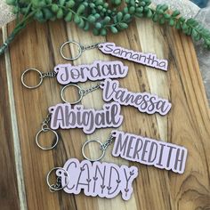 six personalized keychains are sitting on a wooden board next to some plants