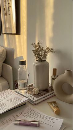 a table topped with books and papers next to a vase filled with flowers on top of it