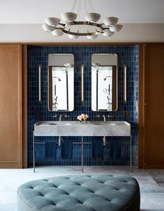 a blue tiled bathroom with two sinks and a round ottoman in front of the mirror