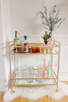 a gold bar cart filled with drinks and condiments on top of a wooden floor