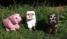 three crocheted animals sitting in the grass next to each other, one pink and one white