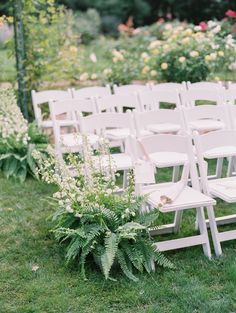 rows of white folding chairs sitting on top of a lush green field next to flowers