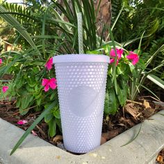 a plastic cup sitting on top of a cement planter filled with pink flowers and greenery