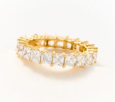 a yellow gold ring with five princess cut diamonds on the side, set against a plain white background