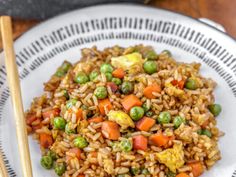 a white plate topped with rice and vegetables next to chopsticks on a wooden table