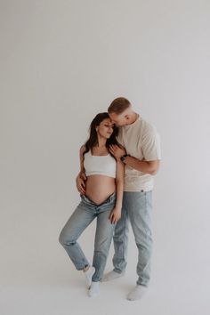 a pregnant couple cuddles in front of a white background