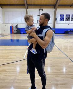 a man holding a small child in his arms on a basketball court with other people