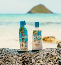 two sunscreens sitting on top of a rock next to the ocean with an island in the background