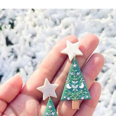 a hand holding two small christmas trees with white stars on them and one is green