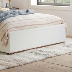 a bed sitting on top of a wooden floor next to a white rug and window