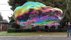 a man is standing in front of a giant kite that looks like a mountain on the street