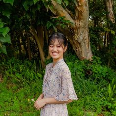 a woman standing in front of some trees and bushes smiling at the camera with her hands on her hips