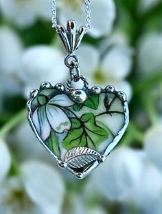 a heart shaped pendant with leaves and flowers in the background, on a silver chain