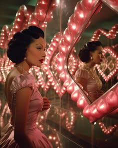 a woman is looking at herself in the mirror while wearing a pink dress and pearls