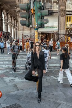 a woman standing in the middle of a street with people walking around and traffic lights above her