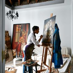 a woman is painting on an easel in the middle of a room with other paintings