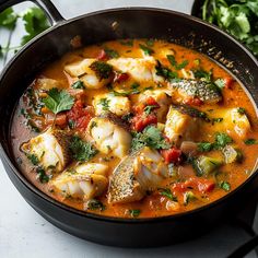 a pan filled with fish and vegetables on top of a counter next to some parsley