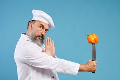 a man holding a knife with an orange on it in front of his face while standing against a blue background