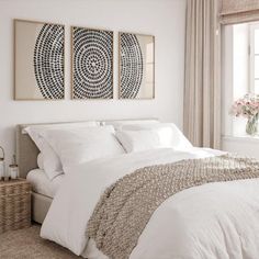 a bedroom with white bedding and two paintings on the wall