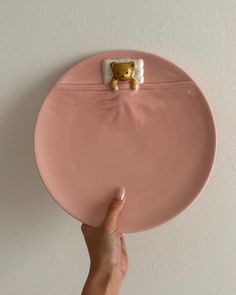 a hand is holding a pink plate with a teddy bear on the front and bottom