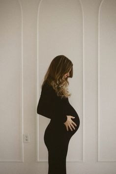 a pregnant woman standing in front of a white wall with her hands on her stomach