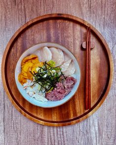 a wooden tray holding a bowl of food and chopsticks