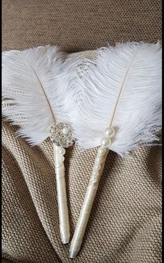 three white feathers are laying on top of a piece of fabric with beads and pearls