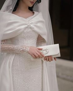 a woman in a white wedding dress and veil holding a clutch on her left hand