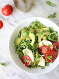 a white bowl filled with lettuce, tomatoes and sliced avocado slices