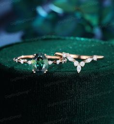 two gold rings with green and white stones on top of a velvet covered hat box