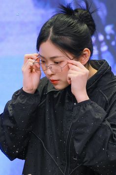 a woman wearing glasses is holding her head to her ear while looking down at something