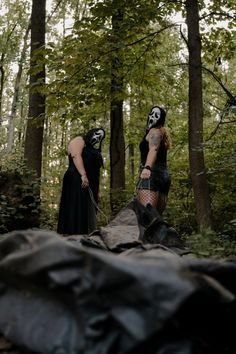 two people dressed in black and white are walking through the woods with masks on their faces