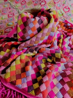 a multicolored knitted blanket on top of a bed with a metal hook