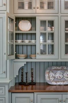 a kitchen with gray cabinets and wooden counter tops, white dishes on the cupboards