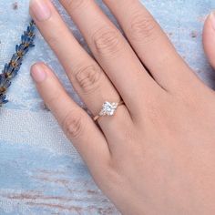 a woman's hand with a diamond ring on it and lavender flowers in the background