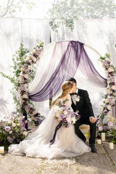 a bride and groom are kissing in front of an altar with purple draping