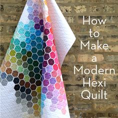 a multicolored hexagonal quilt hanging on a brick wall next to a window