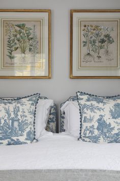 two framed pictures hang above a bed with white linens and blue toilers