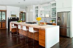 a large kitchen with white cabinets and wooden flooring, along with bar stools