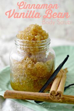 cinnamon vanilla bean body scrub in a glass jar with cinnamon sticks next to it on a green plate