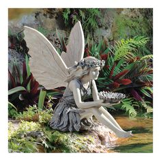 a statue of a fairy sitting on top of a rock next to some water and plants