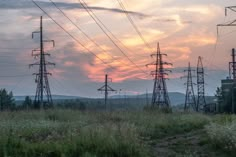 the sun is setting behind power lines in an open field with tall grass and wildflowers