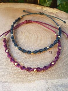 three bracelets with beads on top of a piece of tree trunk in front of green leaves