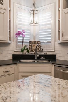 a kitchen with marble counter tops and white cabinets, along with a large flower vase on the sink