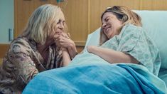 two women in hospital gowns are talking to each other while laying on a bed