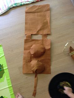 a child is making a paper doll out of brown paper on the floor next to a black plate