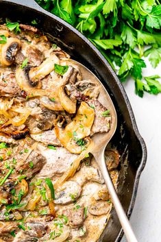 a skillet filled with meat and mushrooms on top of a white table next to parsley