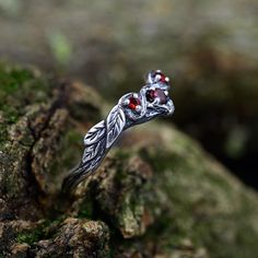 a silver ring with two red stones on top of mossy rocks in the woods